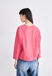 Sudadera de forro polar en rosa desgastado con cuello redondo, mangas raglán y puños de canalé, combinada con jeans de mezclilla azul claro.