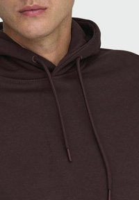 Sudadera marrón oscuro con bolsillo canguro, cordón ajustable y textura de tela suave. Vista en primer plano del escote y los detalles.