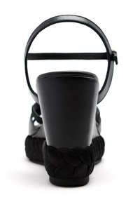 Sandalia cuña negra con parte superior de cuero suave, correa ajustable en el tobillo y una banda de textil trenzado alrededor de la suela.