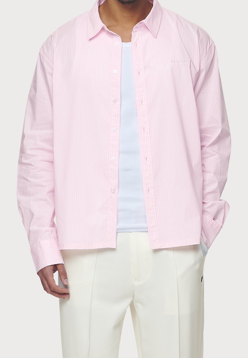 Jasnoróżowa, w paski, koszula zapinana na guziki z klasycznym kołnierzykiem i długim rękawem, z białymi guzikami i luźnym krojem. Nosi się ją na białej bluzce.