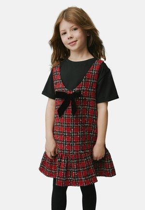 Piros és fekete kockás ruha fodros aljjal, fekete bársonybóbitával, fekete pólóra rétegezve, fekete leggings-szel viselve.