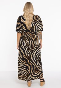 Robe maxi en imprimé animal avec un tissu fluide, présentant une base noire, des rayures beiges et brunes, des manches courtes et une taille cintrée.