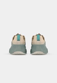 Beige og teal atletiske sko med en struktureret design, rund hæl og kontrasterende trækkrog. Sålen viser mønstrede skridsikre detaljer.