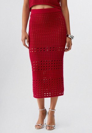 Donna che indossa una gonna midi rossa all'uncinetto e un crop top abbinato con sandali argento con tacco alto e braccialetti argento al polso destro.