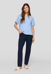 Hellblaues kurzärmliges Oberteil aus strukturiertem Stoff, kombiniert mit dunkelblauen Slim-Fit-Hosen. Das Model trägt weiße Rutschsandalen.