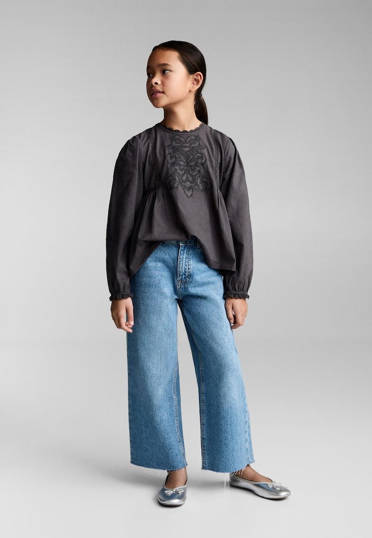 Bluză lungă gri cu mâneci lungi, brodată cu flori, purtată cu blugi largi albaștri și balerini argintii. Design simplu și casual.