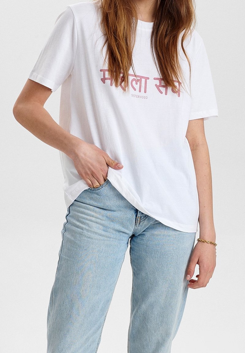 Bílý bavlněný tričko s růžovým nápisem "SISTERHOOD" v angličtině a regionálním písmu. Volný střih s krátkým rukávem.