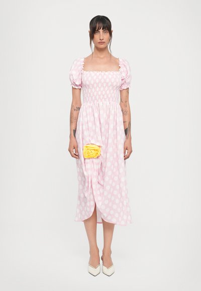 Robe rose à pois avec des manches courtes bouffantes, corsage smocké, longueur mi-mollet, ornée d'une accent en rose jaune sur le devant. Tissu lisse.