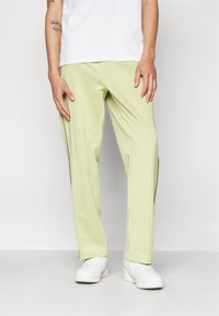 Light green athletic pants with a smooth texture and side slit details, paired with white sneakers and a plain white t-shirt.