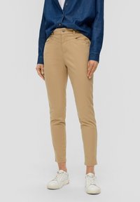 Beige slim-fit byxor med en jämn textur, med en knappstängning och fem fickor. Matchad med vita sneakers och en denimskjorta.