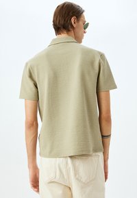 Polo a maniche corte di colore verde chiaro realizzato in tessuto testurizzato. Presenta un colletto e un orlo spaccato, abbinato a pantaloni di colore chiaro.