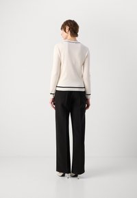 Pull blanc avec des bordures noires au col et aux poignets, associé à un pantalon noir à jambes larges et des talons blancs. La texture semble lisse.