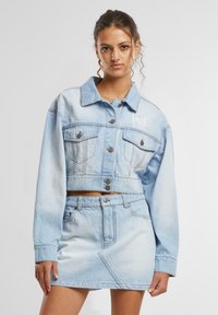 Gaiši zilas džinsa jaka ar īsu dizainu, pogu aizdari un divām krūšu kabatām. Kombinēta ar atbilstošu džinsa mini svārku, kas iezīmē slīpas šuves.