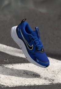 Blue athletic shoe featuring a mesh upper, white sole, black accents, and logo. Rounded toe and lace closure with textured design.