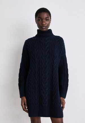 Robe pull bleu marine en tricot avec un haut col, présentant un motif de torsades et des poignets et un ourlet côtelés. Tissu doux et texturé.