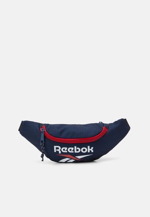 Pungă de fanny din material navy cu fermoar roșu, având logo-ul Reebok și detalii de design în alb și roșu, cu o formă compactă și curbată.