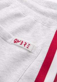 Graue Sweatpants mit einem roten Streifen an der Seite, weicher Textur und einem weißen Etikett mit dem aufgestickten Text "OM3RE" auf der Gesäßtasche.