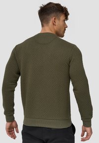 Sudadera texturizada en verde oliva con cuello redondo, puños y dobladillo de canalé, presenta un patrón de gofres en relieve en la tela.