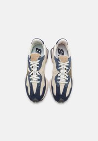 Pár bežových, modrých a olivových sneakers New Balance s bílými tkaničkami, viděných shora na jednobarevném bílém pozadí.