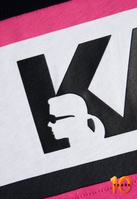 Graphic print featuring a black silhouette profile on white, with bold black letters and a pink and black striped border. Text reads "10 YEARS."