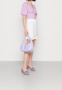 Maglietta viola con maniche a sbuffo, gonna bianca arricciata, borsa lavanda e tacchi intrecciati lavanda. Texture lisce con una palette di colori coerente.