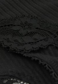 Tessuto nero con un motivo testurizzato e un orlo in pizzo, che presenta bordi scallop e dettagli nei disegni tessuti.