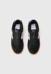 Black suede sneakers with white accents, round toe, rubber sole, and flat laces, displaying a clean, modern design from a top view.