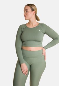 Olivgrünes, geripptes Cropped-Top mit langen Ärmeln und rundem Ausschnitt, kombiniert mit passenden, hochgeschnittenen Leggings mit seitlichen Details.