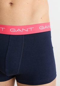 Navy blauwe katoenen boxershorts met een roze elastische tailleband waarop het GANT-logo herhaaldelijk is afgebeeld. Gladde textuur met een aansluitend ontwerp.