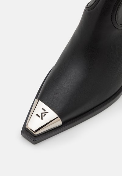 Zwarte leren enkelboot met een spitse neus en een metalen zilveren kap met logo-details. Gladde textuur en slank design.