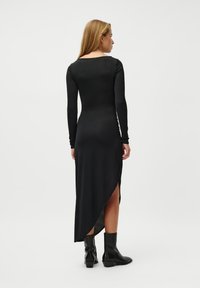 Μαύρο φόρεμα με μακριά μανίκια και ραβδωτή υφή, με υψηλή σχίση στη μία πλευρά και στρογγυλή λαιμόκοψη στο πίσω μέρος, συνδυασμένο με μαύρες μπότες μέχρι τον αστράγαλο.