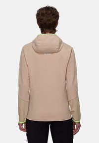 Beige technische Jacke mit strukturierter Oberfläche, Kapuze und kontrastierenden beigen Ärmeln. Mit neon-grünen Akzenten und einem Logo auf der Rückseite.