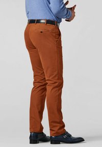 Bruine katoenen broek met een smalle pasvorm, zijzakken en een achterzak; gecombineerd met zwarte leren schoenen en een lichtblauw overhemd met lange mouwen.