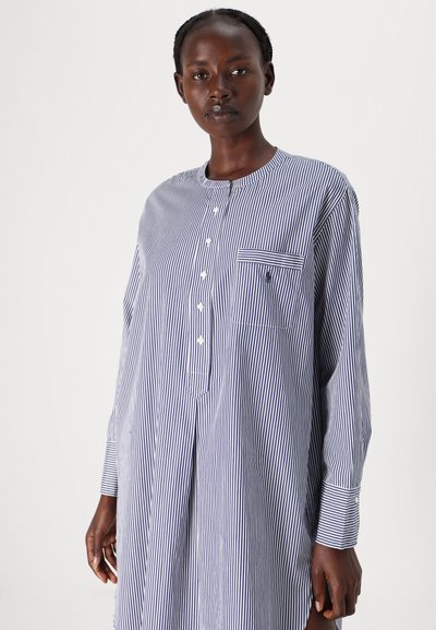 Camisa de botões riscada em azul-marinho e branco. Possui mangas longas, um bolso no peito e um decote redondo. Tecido leve com uma textura suave.