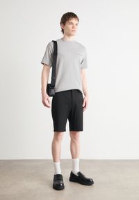 T-shirt gris à manches courtes, shorts noirs, chaussettes blanches mi-mollet et chaussures noires à enfiler. Les accessoires comprennent un petit sac messager noir.