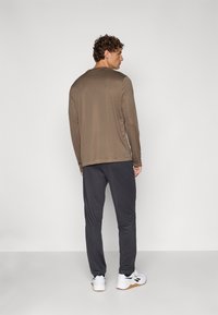 Brūns garās piedurknes krekls, kas apvienots ar tumši pelēkiem biksēm. Krekls ir ar vienkāršu dizainu un apaļu apkakli. Baltas sporta kurpes pabeidz tēlu.