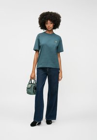 Σκούρο teal βαμβακερό t-shirt με κοντά μανίκια, σετ με φαρδιά τζιν παντελόνια σε σκούρο μπλε. Ένα μικρό πολύχρωμο λογότυπο βρίσκεται στο στήθος.