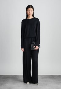 Svart to-delt antrekk med en langermet topp og vide bukser, laget av teksturert stoff. Inkluderer en liten svart clutch-veske.