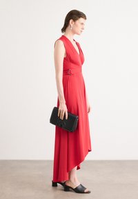 Robe midi rouge avec un décolleté en V et des manches courtes, cintrée à la taille par une bague argentée. Associée à une pochette noire DKNY et des sandales à glissière noires.