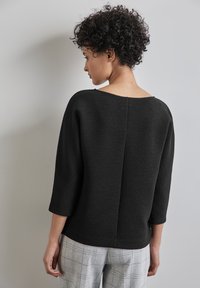 Zwart textuur top met driekwart mouwen en een brede halslijn, voorzien van een middennaad en een relaxed fit, gecombineerd met grijs geruite broek.