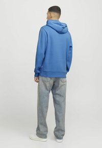 Sudadera azul de tejido suave con un corte holgado, que presenta una capucha grande y puños acanalados, combinada con pantalones vaqueros holgados de color gris claro y zapatillas blancas.