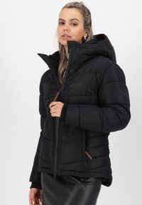 Giacca a vento nera con chiusura a zip, капuccio e polsini elastici. Presenta un design trapuntato e un accento in pelle marrone sul lato.