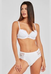 Baltos spalvos apatinio trikotažo komplektas, kuriame yra paminkštinta liemenėlė su banguotomis kraštelėmis ir derančios aukšto liemens kelnaitės su nėriniais šonuose ir dekoratyviniu apvadu.