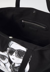 Fekete vászontáska belső cipzáros zsebbel, az egyik oldalán napszemüveges figura grafikai mintázattal.