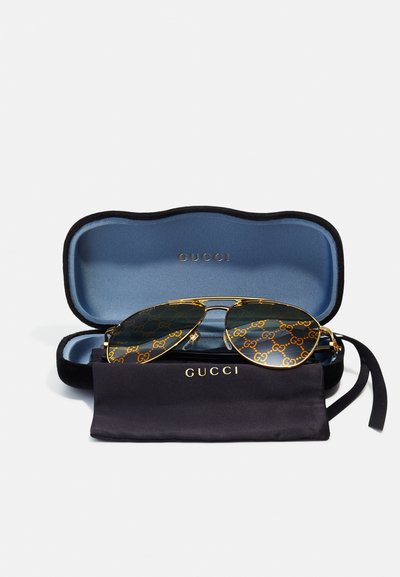 Occhiali da sole Gucci in un astuccio nero con interno blu. Montatura dorata, lenti scure con motivo del logo GG e un panno per la pulizia nero.