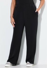 Zwarte wijde broek met een elastische tailleband, met zijzakken en een gladde stoftextuur. Gekleed met sprankelende witte sneakers.