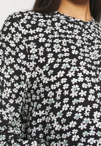 Blusa negra con estampado de flores en blanco y verde menta. Fabricada en un tejido suave, con cuello redondo y mangas largas.