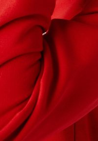 Tessuto rosso con una superficie liscia, caratterizzato da pieghe drappeggiate. Il materiale sembra elastico e morbido, con un colore ricco e vibrante.