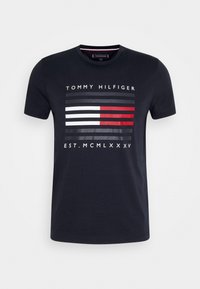 Camiseta de algodón azul marino con un diseño gráfico de rayas horizontales en rojo, blanco y gris, con el texto "TOMMY HILFIGER EST. MCMLXXXV".