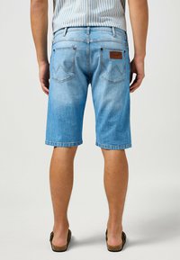 Shorts de mezclilla azul claro con corte recto, diseño de cinco bolsillos y un parche de cuero en la parte trasera de la cinturilla que presenta costura en zigzag.